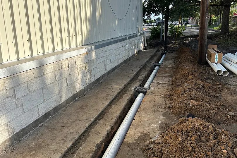 Channel drain and pipe run along the side of a commercial building