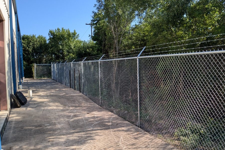 Chain link fence running beside a commercial building and driveway