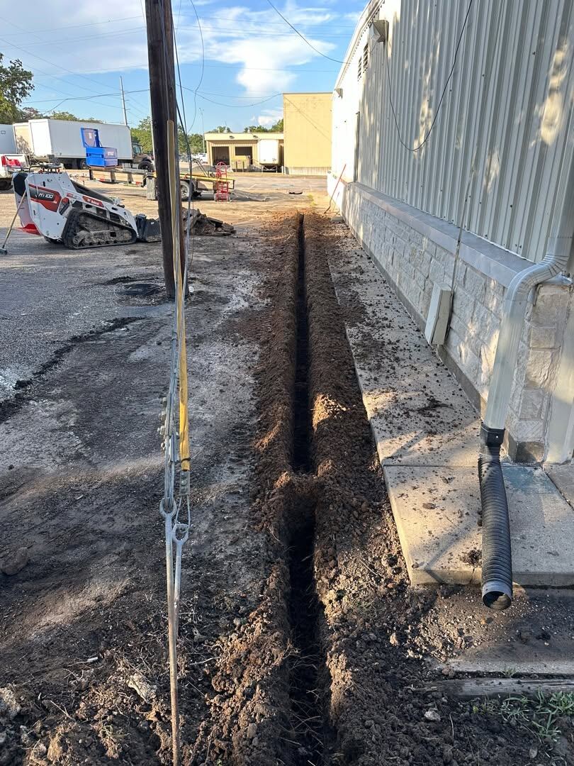 Drainage line trenched into asphalt alongside a commercial building