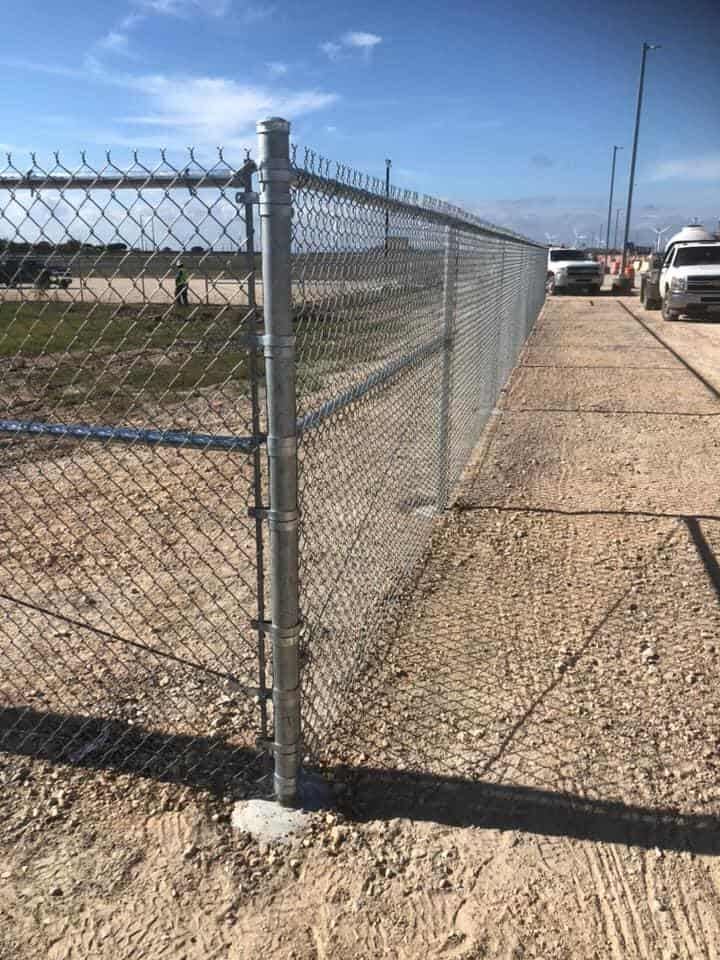 Chain link perimeter fence along a commercial yard with work trucks behind it