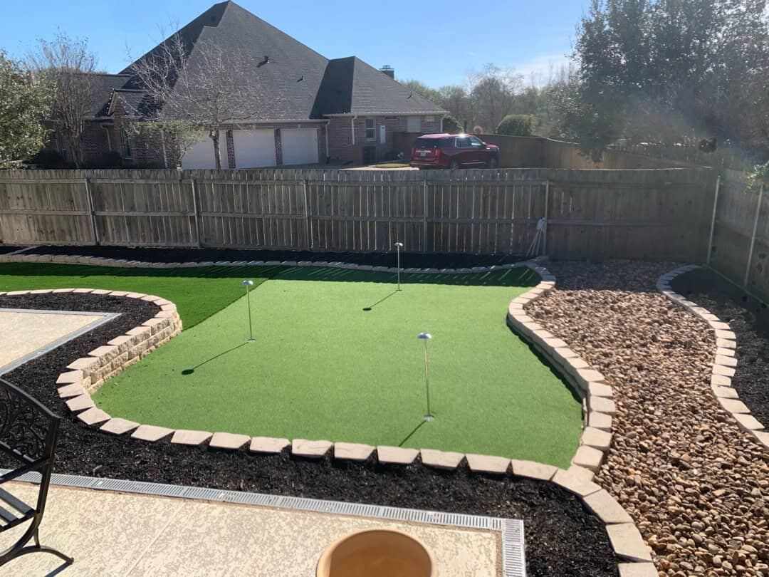 Backyard artificial turf putting green with brick edging and mulch beds
