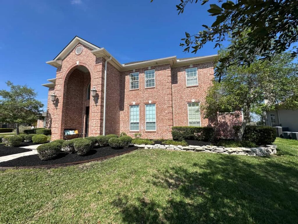 Two-story brick home in Bryan, TX with freshly mown lawn, trimmed shrubs and clean dark mulch beds maintained by Lone Star